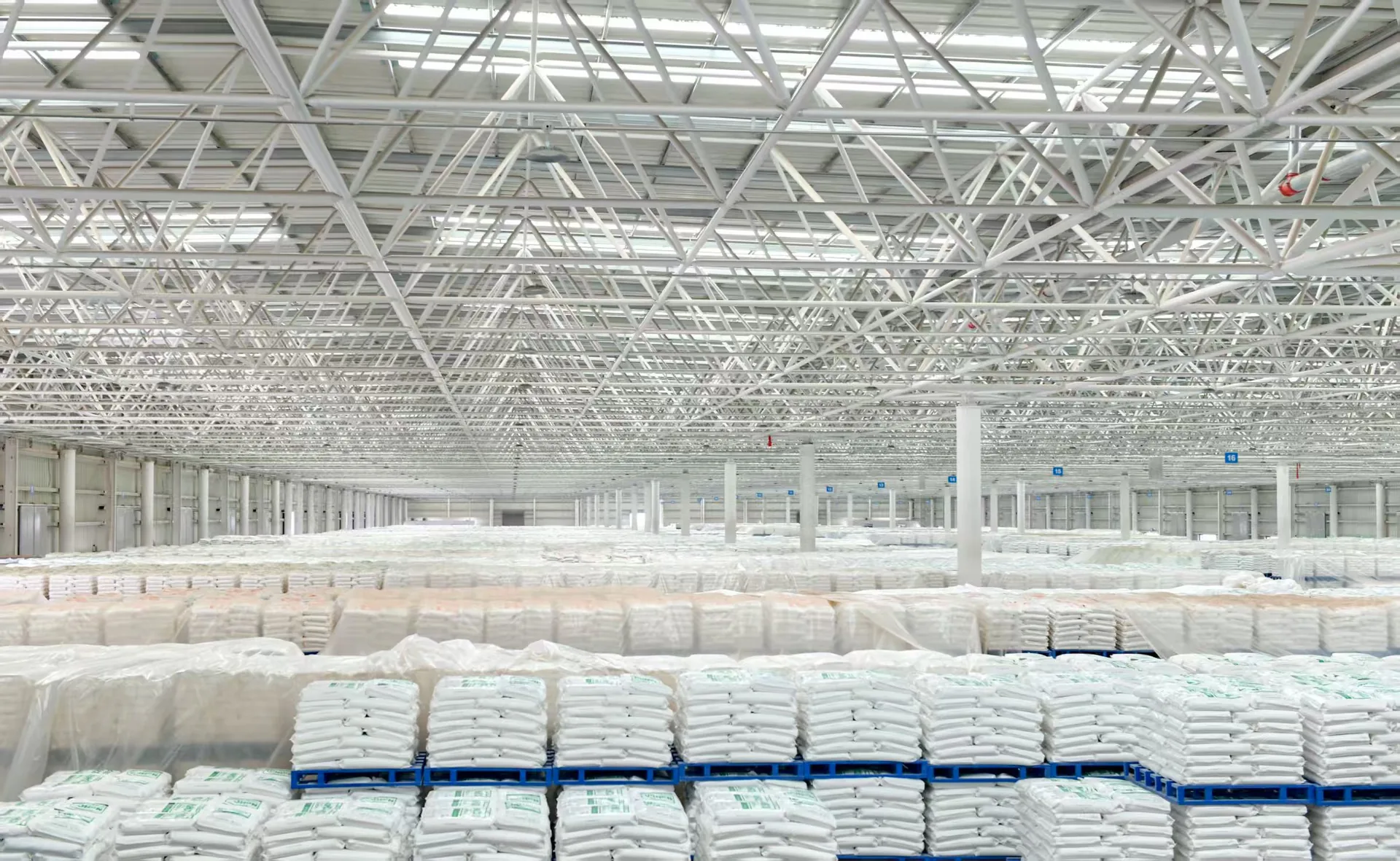Finished-goods warehouse at the Alxa Yingen producing plant, palletised bags in the foreground and plastic-wrapped jumbo bags stored in rows under the steel roof